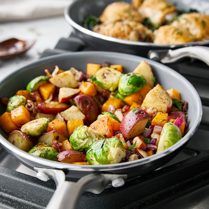 Shrimp and mixed vegetables cooking in a gray ceramic nonstick skillet from a multi-piece cookware set.