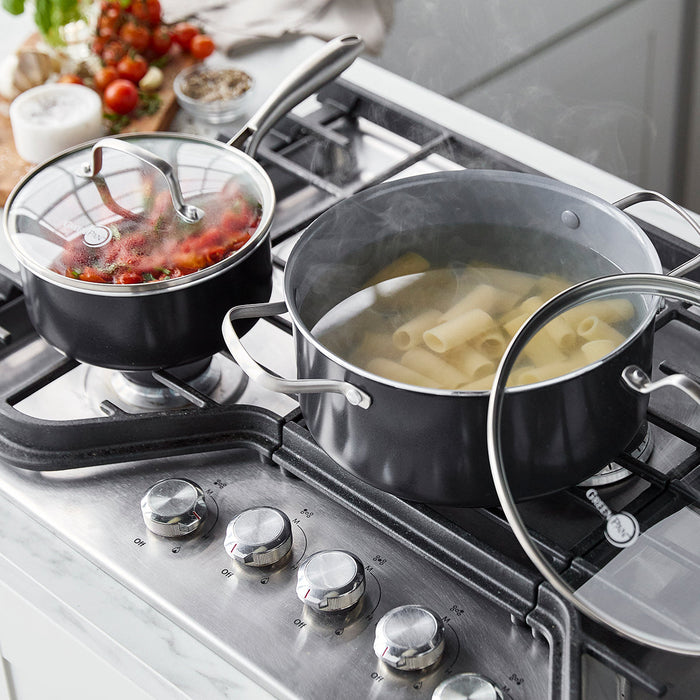 Swift Ceramic Nonstick 12-piece cookware set in use, cooking pasta, tomato sauce, and shrimp on a stovetop.
