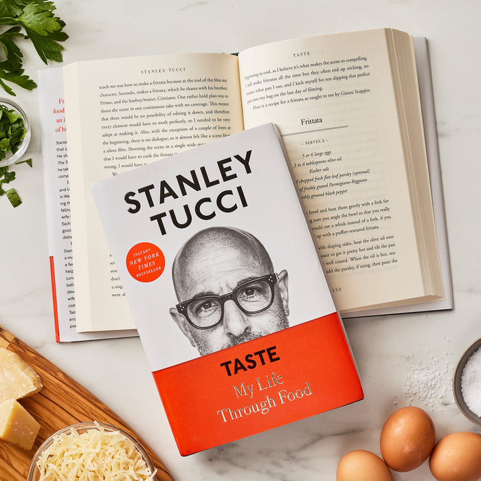 Stanley Tuccis Taste: My Life Through Food cookbook on a table with Italian recipes and an open book in the background.