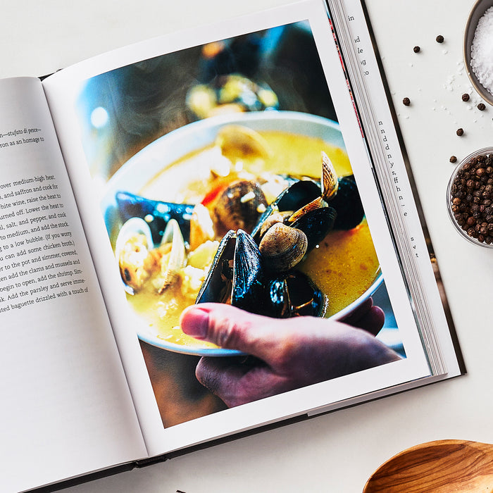 Open cookbook displaying seafood stew, with salt and pepper shakers and a wooden spoon nearby on the table.