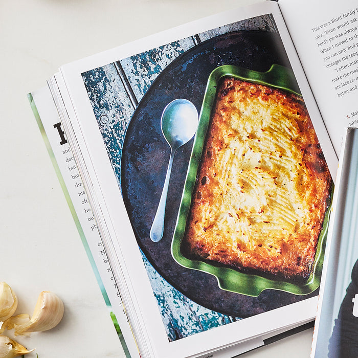 Baked casserole in a green dish with garlic cloves beside it, from The Tucci Table Cookbook.
