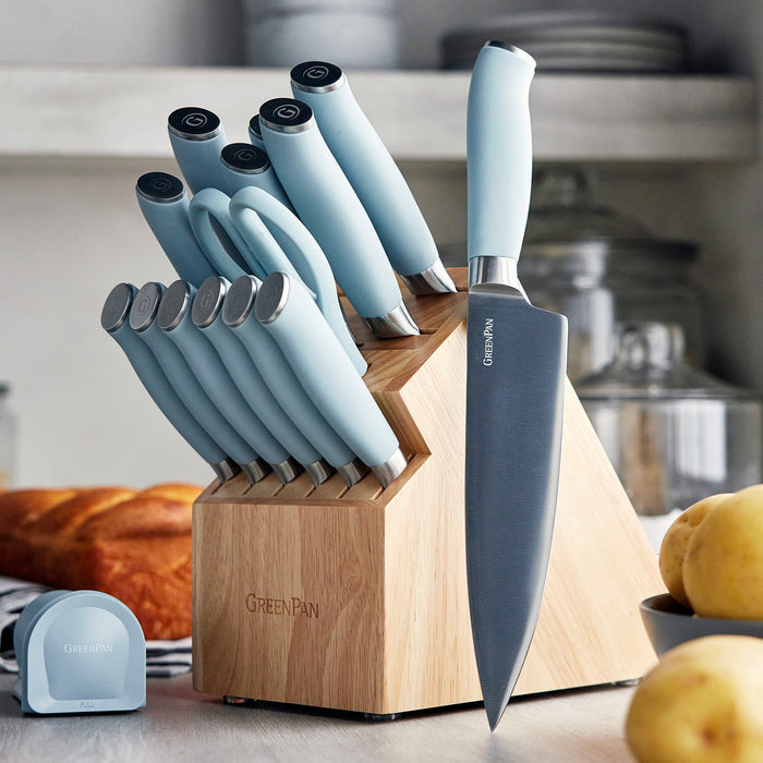16-piece blue titanium knife block set on a kitchen counter with bread and potatoes nearby.