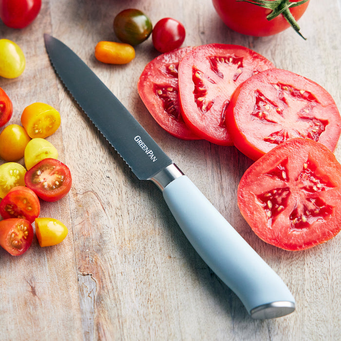 Blue serrated knife with tomatoes on a wooden surface, from the Titanium Cutlery 16-piece set.