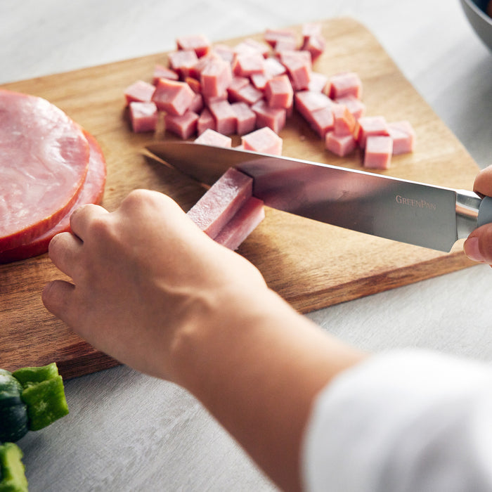 Knife from Titanium Cutlery 16-piece set in Blue Haze slicing ham on a cutting board.