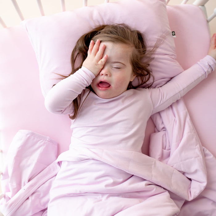 Young girl stretching in bed underneath the Toddler Blanket in Thistle 1.0 with her head resting on a toddler pillow in matching pillowcase