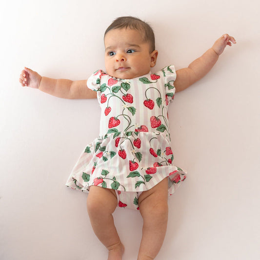 Young infant wearing the Twirl Bodysuit Dress in Strawberry Fields laying on a light pink blanket