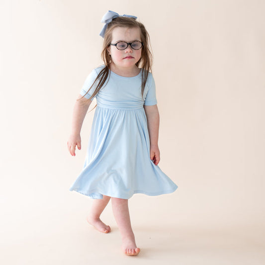 Young girl wearing a light blue dress and glasses on a plain background