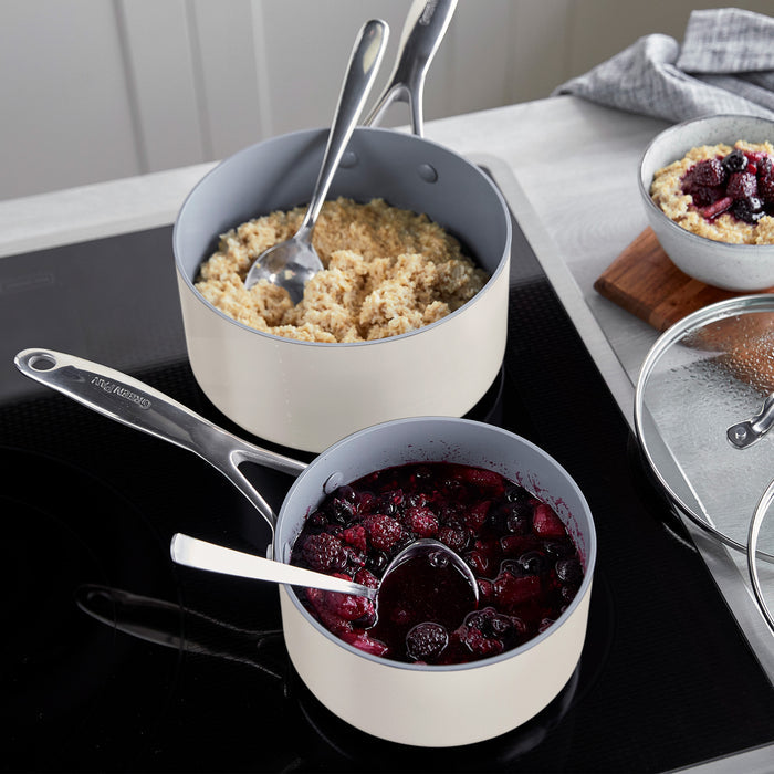 Two grey ceramic saucepans with lids, one filled with quinoa and the other with berry compote. Set of two.