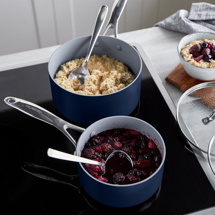 Two twilight blue ceramic nonstick saucepans with lids on a stovetop, part of a matching set.