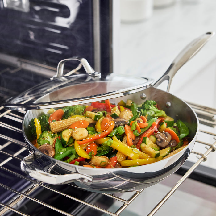Stainless steel wok with lid on oven rack, filled with assorted sautéed vegetables.