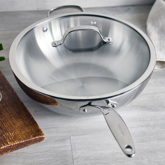 Stainless steel 12-inch wok with matching lid on a light gray countertop.
