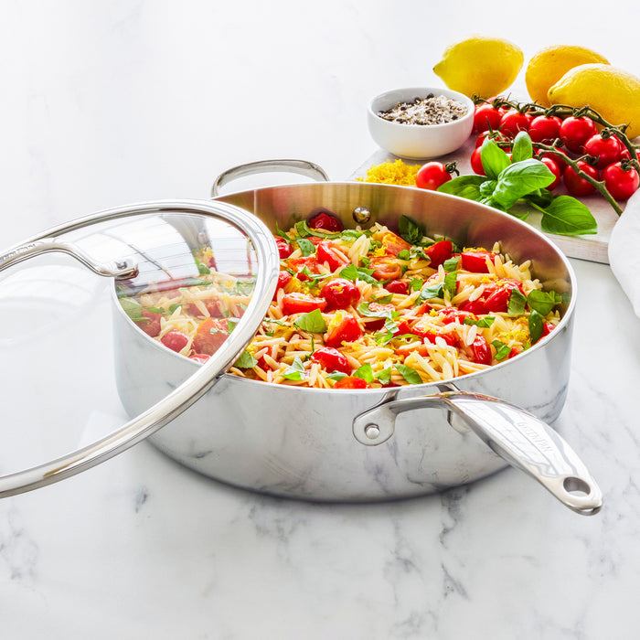 Stainless steel sauté pan with lid, 5-quart size, with pasta, tomatoes, basil, and cheese on a marble countertop.