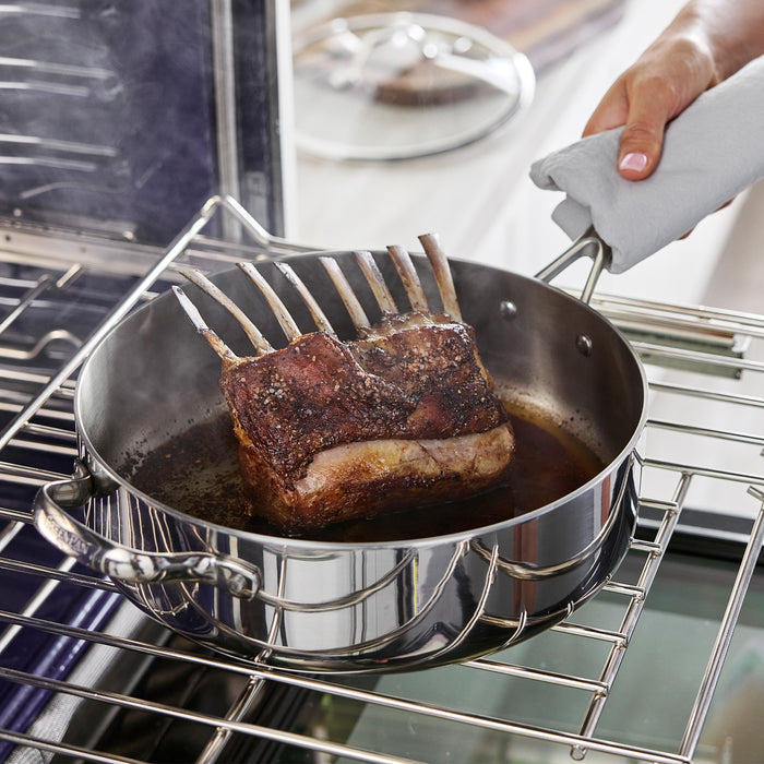 Rack of lamb cooking in a stainless steel 5-quart sauté pan with lid on an oven rack.