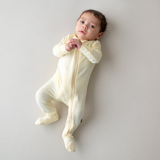 Baby in a yellow-colored zippered footie lying on a light gray background