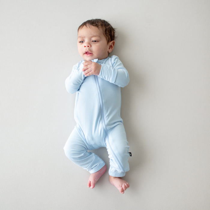 Baby wearing a light blue zippered romper on a plain background