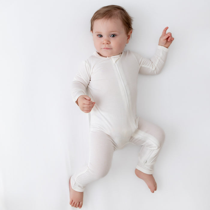 Baby laying on a Cloud surface with one hand up and wearing a Zippered Romper in Cloud