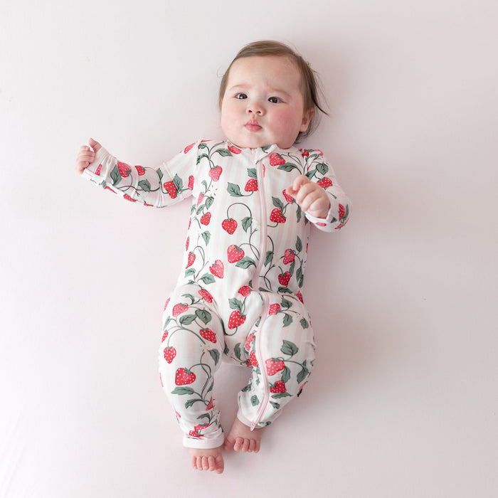 Infant laying on a light pink surface wearing the buttery soft Zippered Romper in Strawberry Fields